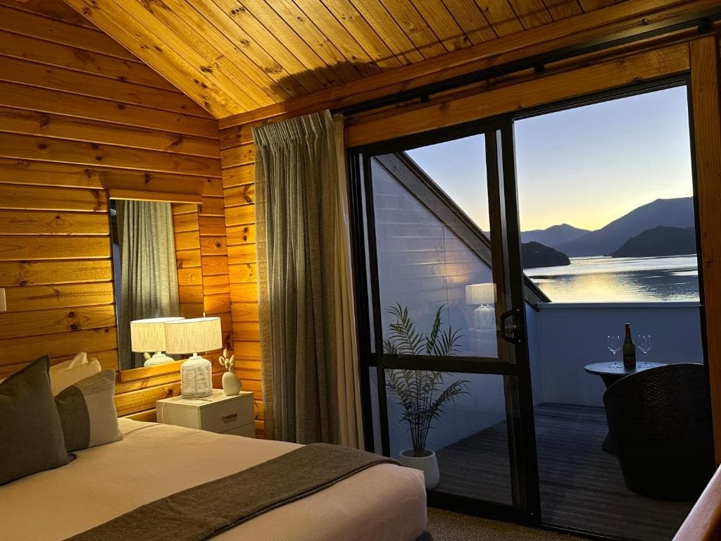 Wooden cabin bedroom with sliding glass door opening to balcony and water view
