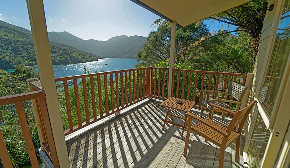 Balcony with wooden chairs and table overlooking water and mountains at Punga Cove
