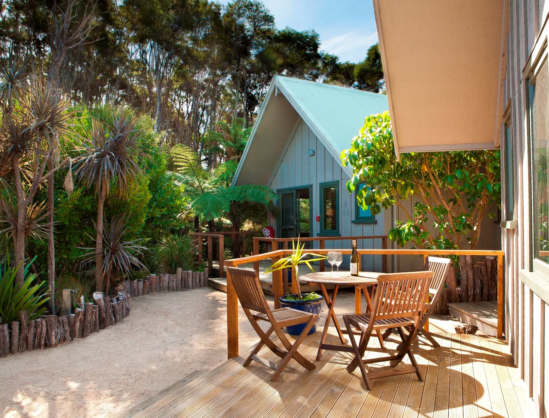 Wooden lodge and outdoor deck with table and chairs surrounded by native forest and ferns