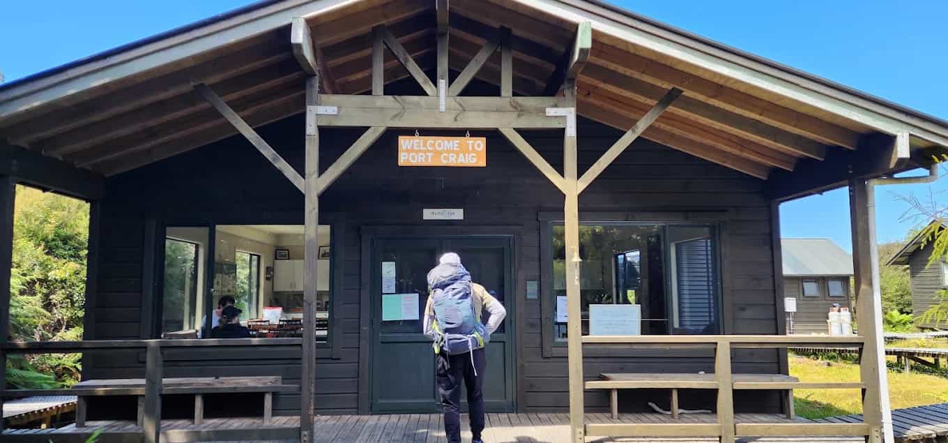 Hiker with backpack standing at entrance of Port Craig Lodge with wooden porch