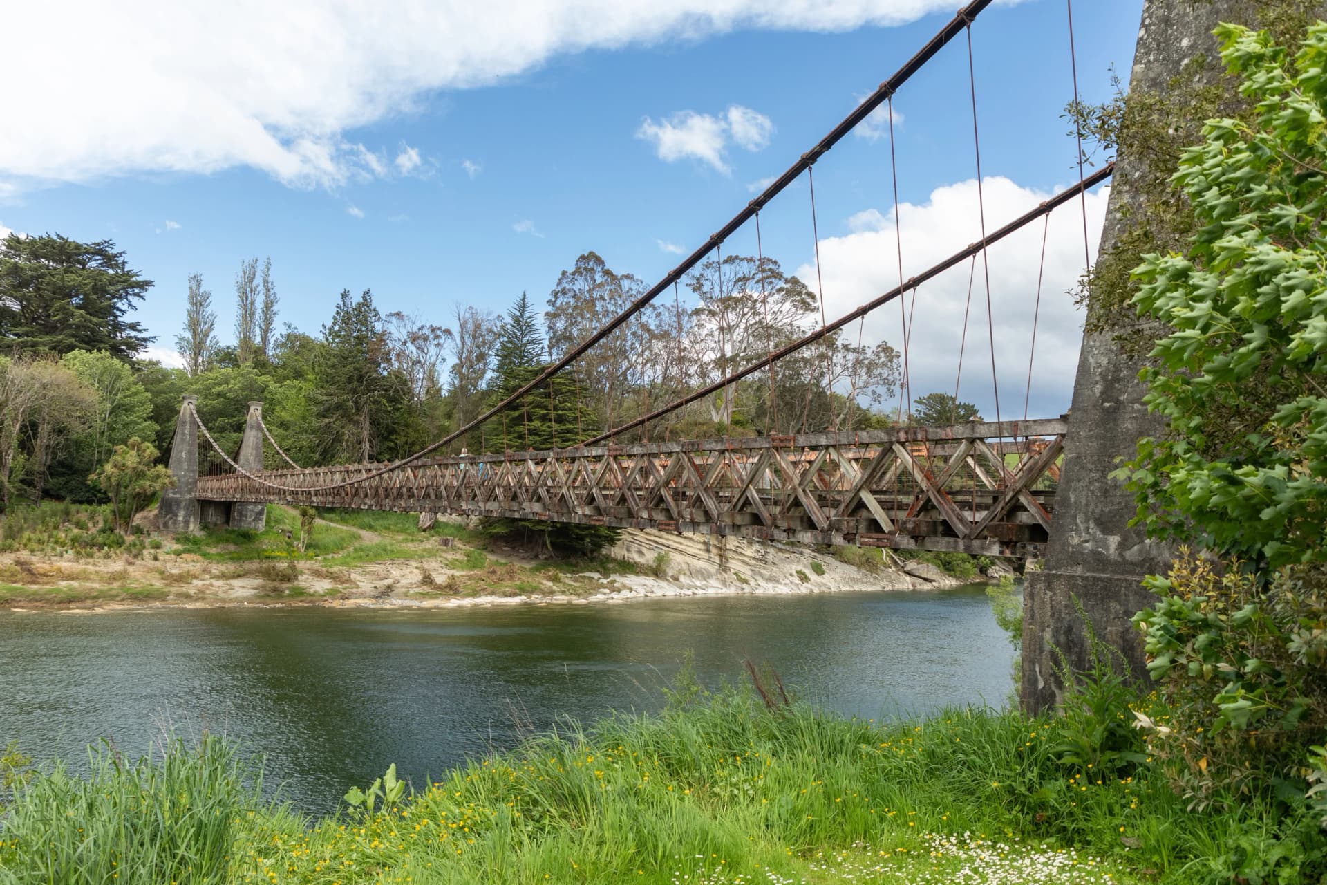 The Clifden suspension bridge, dating to 1899, spans the Waiau river north of Tuatapere, Southland, New Zealand. The 111.5 m bridge features a plaque commemorating district men killed in World War 1.